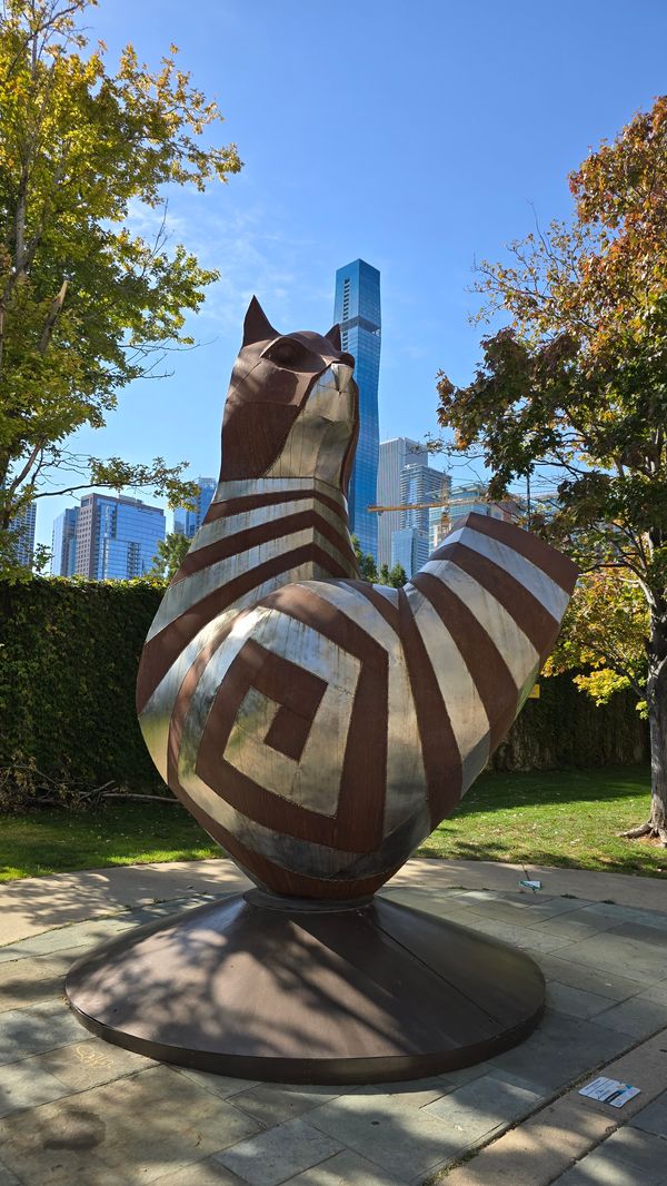 An outdoor statue of a stylized, angular Chesire Cat. The background is a part of Chicago's skyline.