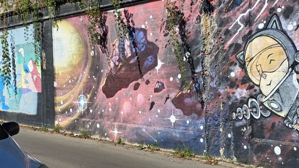 Another portion of the previous graffiti wall, with the corgi in a spacesuit to the right, centered on a painting of rocks floating in space near a glowing yellow star.