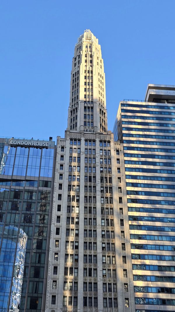 A tall, thin, light brick building with many windows, an a top, hexagonal section (only 3 sides are visible).