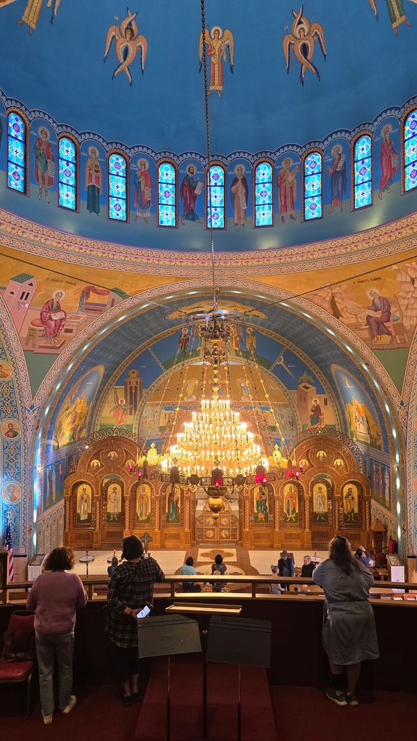 A picture from the balcony of a Ukrainan Church, showing an ornately painted dome, building walls, and a lit chandelier.