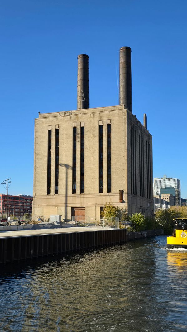 A concrete or brick building labeled 301 Taylor with two smoke stacks and tall, thin windows