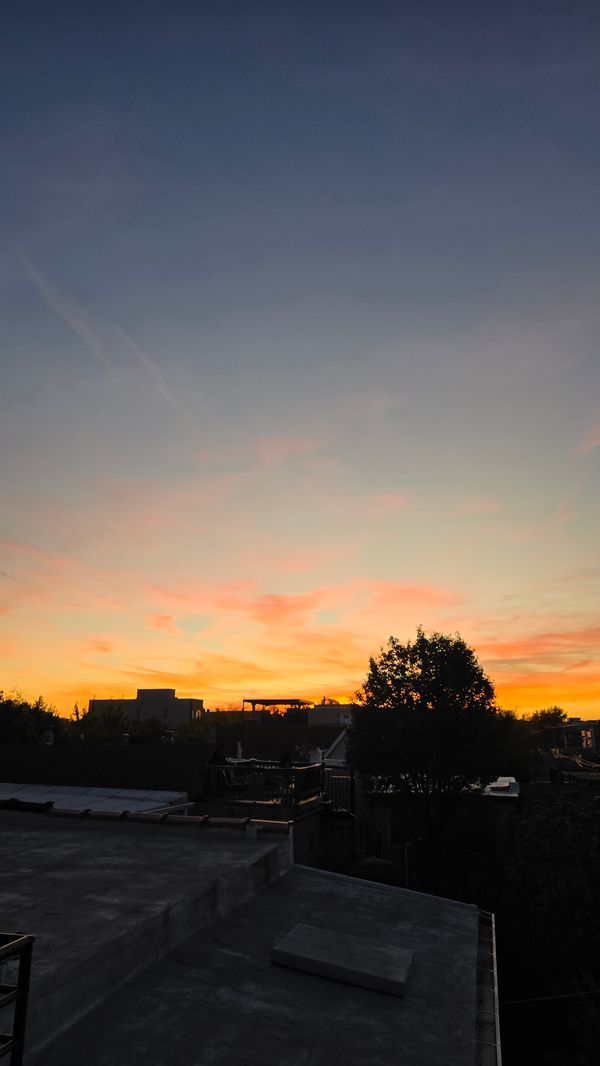 A vertical shot of a deep yellow and orange sunset from the balcony of an apartment building. Other buildings and trees are in silhouette, with slight orange highlights.