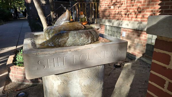 A metal statue of a coil of poop on a concrete pedestal labeled 'SHIT FOUNTAIN'