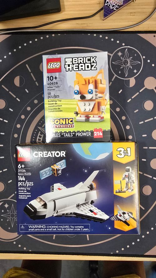 A picture of two Lego Sets on a celestial mouse mat: 1 is a Lego Brick Heads model of Miles 'Tails' Prower, the other is a Lego Creator Space Shutter that can also be assembled into an astronaut and a space fighter.