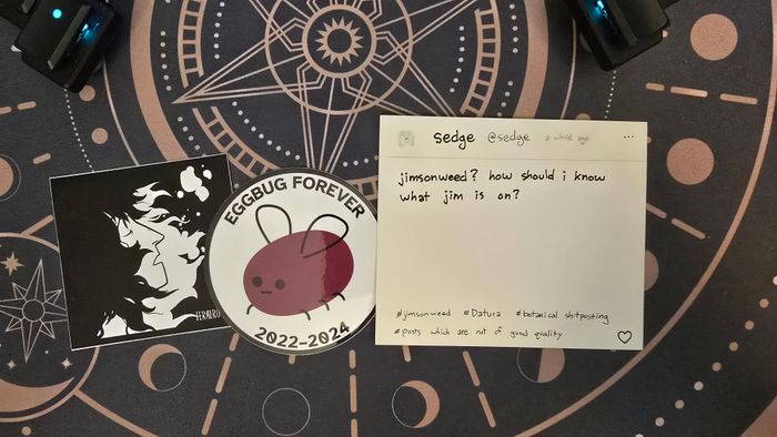 a photo of two stickers and a postcard. One sticker has a black and white picture of a long-haired person, with the text 'FERALROYAL', partially obscured. The sticker in the middle is round and has a picture of eggbug, and written around it is 'EGGBUG FOREVER' and '2022-2024', The post card is a handwritten post from @sedge: 'jimsonweed? how should i know what jim is on?' with tags: '#jimsonweed, #datura, #botanical shitposting, #posts which are not of good quality'