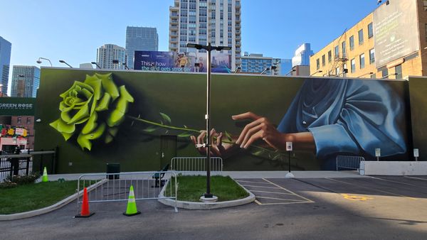 A wide mural of a person, dressed in draping blue fabric, holding a green rose. The building is labeled 'Green Rose Dispensary'